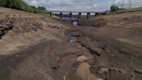 A bare reservoir bed with a bridge in the background