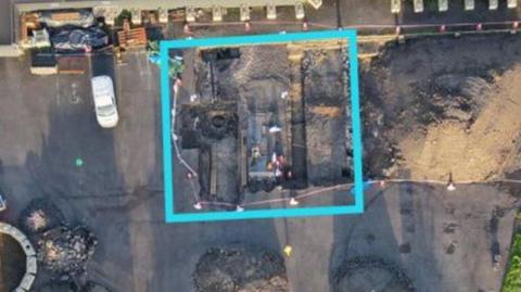 An aerial map of the site shows an an area marked by a blue square. Various areas of the site have been dug up and there is machinery carrying out the digs.