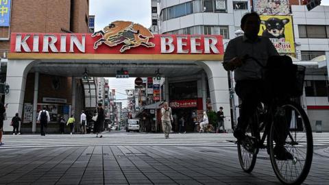 A man riding a bicycle, with a building behind him that reads: Kirin Beer