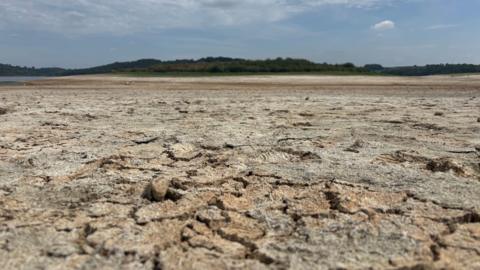 Carsington Water reservoir dry and cracking under a blue summer sky