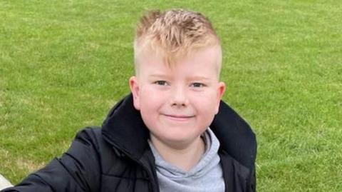 A child, George Fox, wearing a black coat and smiling at the camera.