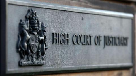 A grey sign at the High Court in Edinburgh which reads 'High Court of Justiciary'.