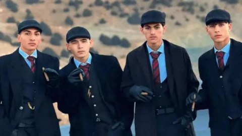 Four Afghan men in three piece suits and flat caps hold cigars
