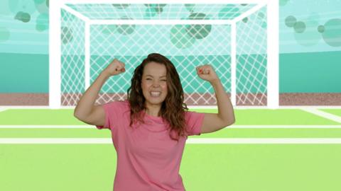 Evie Pickerill in a pink t shirt dancing on a football pitch with her arms raised in the air.