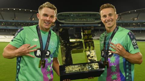 Oval Invincibles players Sam Curran (left) and Tom Curran (right) hold up The Hundred trophy and three fingers each after their side made it three straight title wins
