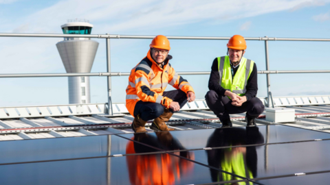 A wide shot of Chris Ambler and Matt Thomas crouching on solar panels.