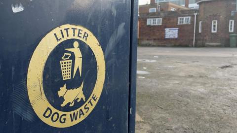 A black bin has the words litter and dog waste in gold with a logo of a dog