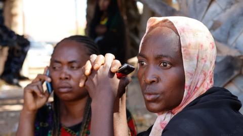 Two women, who are parents of kidnapped schoolchildren wait outside St Mary's Private Catholic School in Papiri