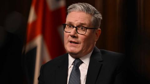 Keir Starmer looks left of camera wearing glasses and suit in front of a UK flag while speaking during Sunday with Laura K on Sunday.