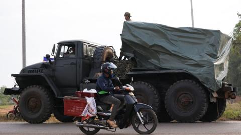 Man driving motorcycle past a military truck