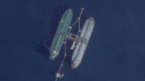 An overhead view of two oil tankers at sea, docked next to a pipe