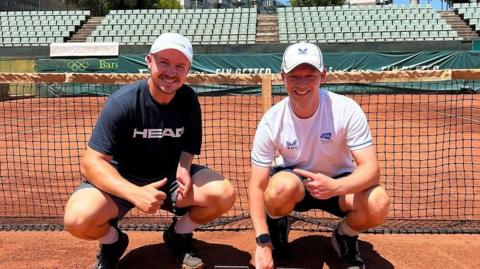 Matt Grover and Ross Cudmore on a clay court in Barcelona smiling by the net.