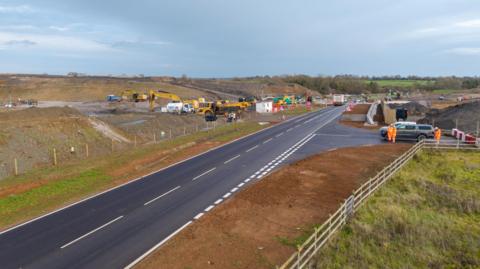 A view of the realigned B4525 on an overcast day. Work crews are pictured beside the freshly laid tarmac.
