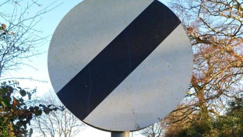 Traffic sign for maximum speed 60 on an empty provincial road, wild vegetation and trees with green foliage against the sky.