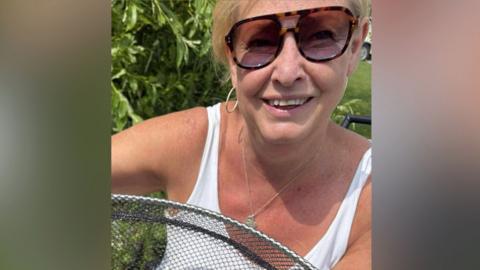 A woman with blonde hair and sunglasses smiles for the camera.