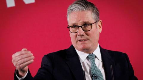Sir Keir Starmer gives a speech in front of a red backdrop.