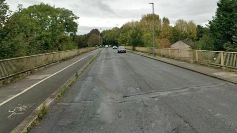 A Google Streetview screenshot of the viaduct on Eastern Way in Carlisle. The single-carriage road has a footpath on one side and a footpath and cycle lane on the other, with a metal parapet.