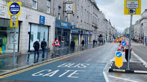 Bus gate sign on the road in Aberdeen with shops up both sides of Union Street