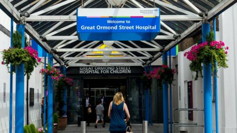 A woman walks under a blue and white sign for Great Ormond Street Hospital in its entrance.