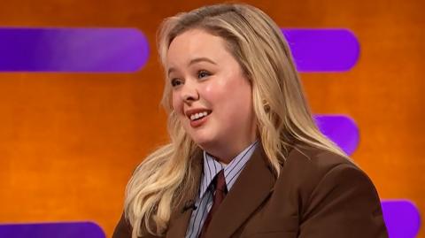 Nicola Coughlan wears a suit and tie, she has long blonde hair.