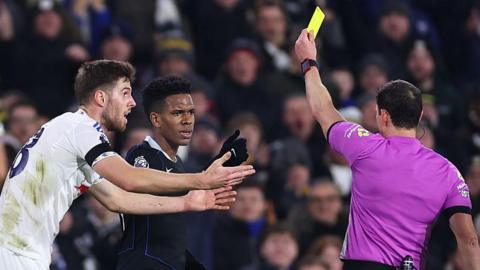 Estevao Willian looking angry as he receives a yellow card from referee Darren England at Elland Road