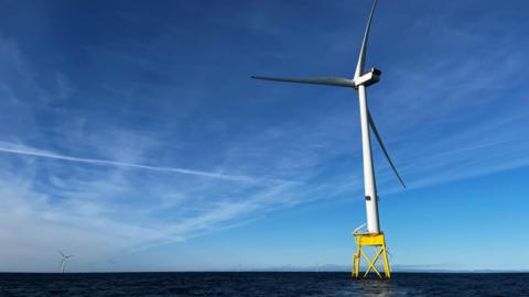 A single wind turbine sits on a yellow platform in the waters of the North Sea with a few other turbines in the background