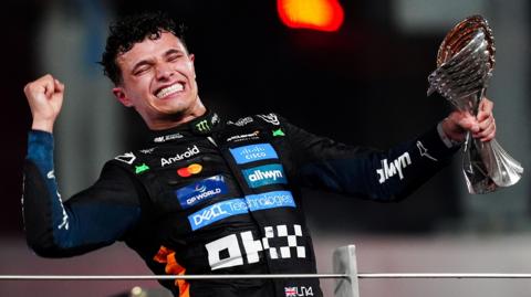 Lando Norris closes his eyes and appears to yell in celebration, while holding his third-place trophy, after winning the F1 drivers' title in the Abu Dhabi Grand Prix