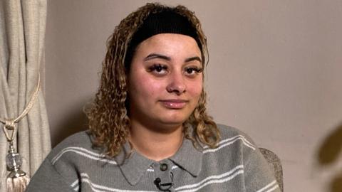 Kayla Palmer pictured with blonde curly hair and a black thick headband. She has a silve nose ring and is wearing a grey jumper.