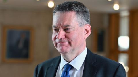 Murdo Fraser, who has short grey hair, wearing a dark suit, white shirt and blue tie.