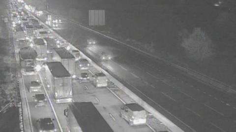 Traffic queuing on four-lane motorway carriageway - heading away from the camera. Traffic is flowing on the other carriageway.