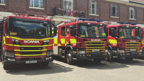 A row of three fire engines outside of a brick building