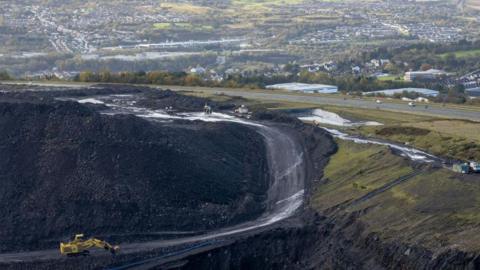 The edge of the main mining void at Ffos y Fran opencast coalmine. Beyond which the A4060 + homes and businesses in Merthyr Tydfil are visible.