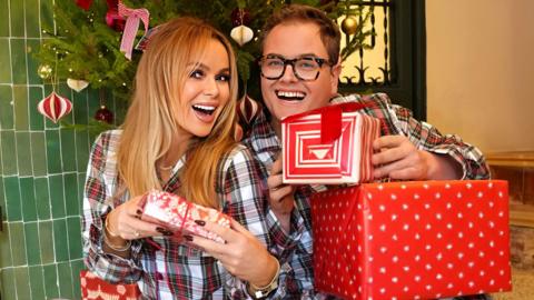 Amanda Holden and Alan Carr excitedly hold up red and white Christmas presents to the camera