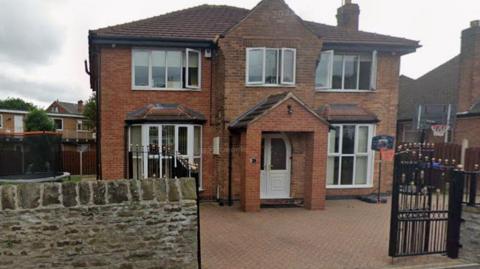 The outside of two-storey house. It features a brick archway over the front door and some black gates at the edge of the driveway.