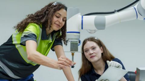 Female engineers performing collaborative robotic operation training in smart factory one controlling robotic machine other observing process teamwork focus in hands-on automation skill lab