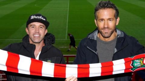 Rob Mac and Ryan Reynolds hold a red and white football scarf