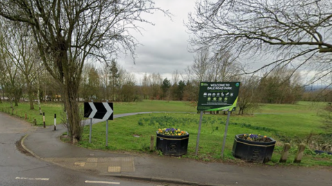 A sign which reads Dale Road Park in front of a green space, with trees in the distance and grey sky above