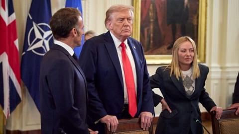 Donald Trump is pictured standing by a desk with Giorgia Meloni and Emmanuel Macron