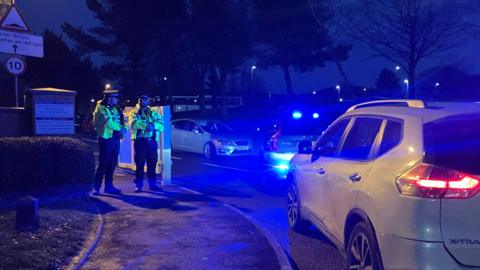 Two policemen stood outside the school property on the pavement surrounded by cars