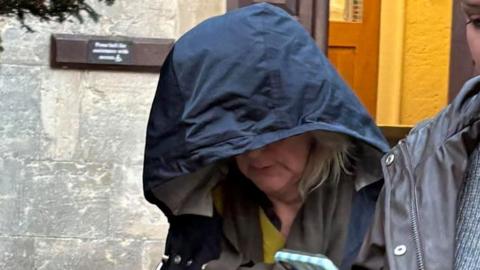 Jane Barnard looks to the ground as she leaves Gloucester Crown Court, her face is obscured by the navy blue hood of a rain jacket.