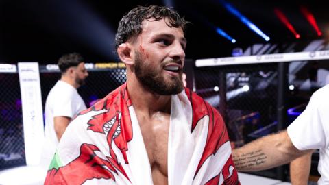 MMA fighter Levi Batchelor smiling and holding a Welsh flag over his shoulders.
