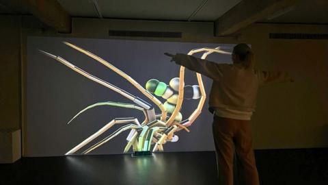 Person standing with their arms out in front of a screen with a futuristic sea creature.