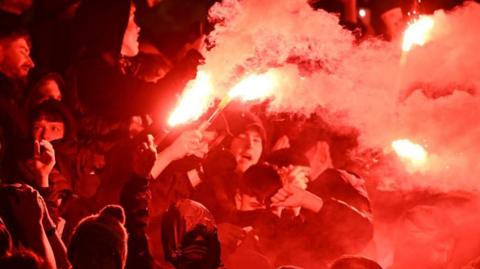 Hooded Aberdeen fans setting off pyrotechnics during a match between Dundee United and Aberdeen in Dundee