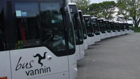 A large carpark which has a row of modern silver buses, it reads bus vannin on the side of them.