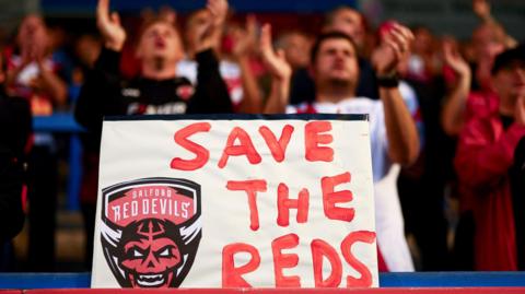 A 'Save the Reds' sign is held up by Salford Red Devils fans during last season