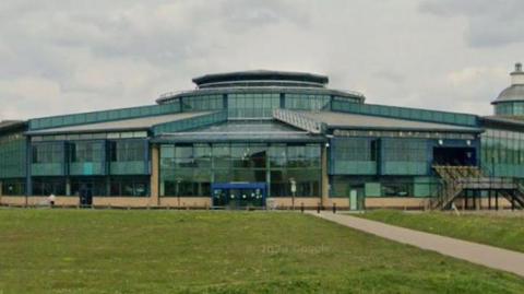 Exterior of the shopping centre- a green glass building with grass in the front.