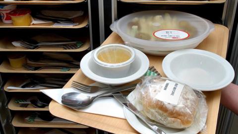 A person removes a hospital meal from a rack of trays