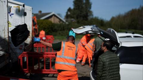 A worker throws a bin bag inside a bin lorry of a Mobile Household Waste Centre where residents dispose of their rubbish