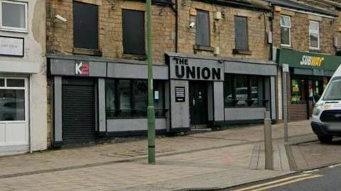 A Google Street View of K2 and The Union in Consett. The two units are next to each other on the lower levels of terraced buildings, flanked by other shops and commercial units, including Subway. Both have grey panelling around the windows and doors where the shop signs are displayed.