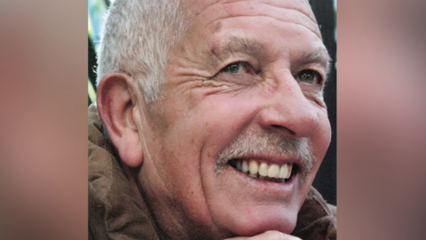 A smiling Geoff King looks up at a point above the camera. He has white hair and a moustache and wears a brown corduroy jacket.